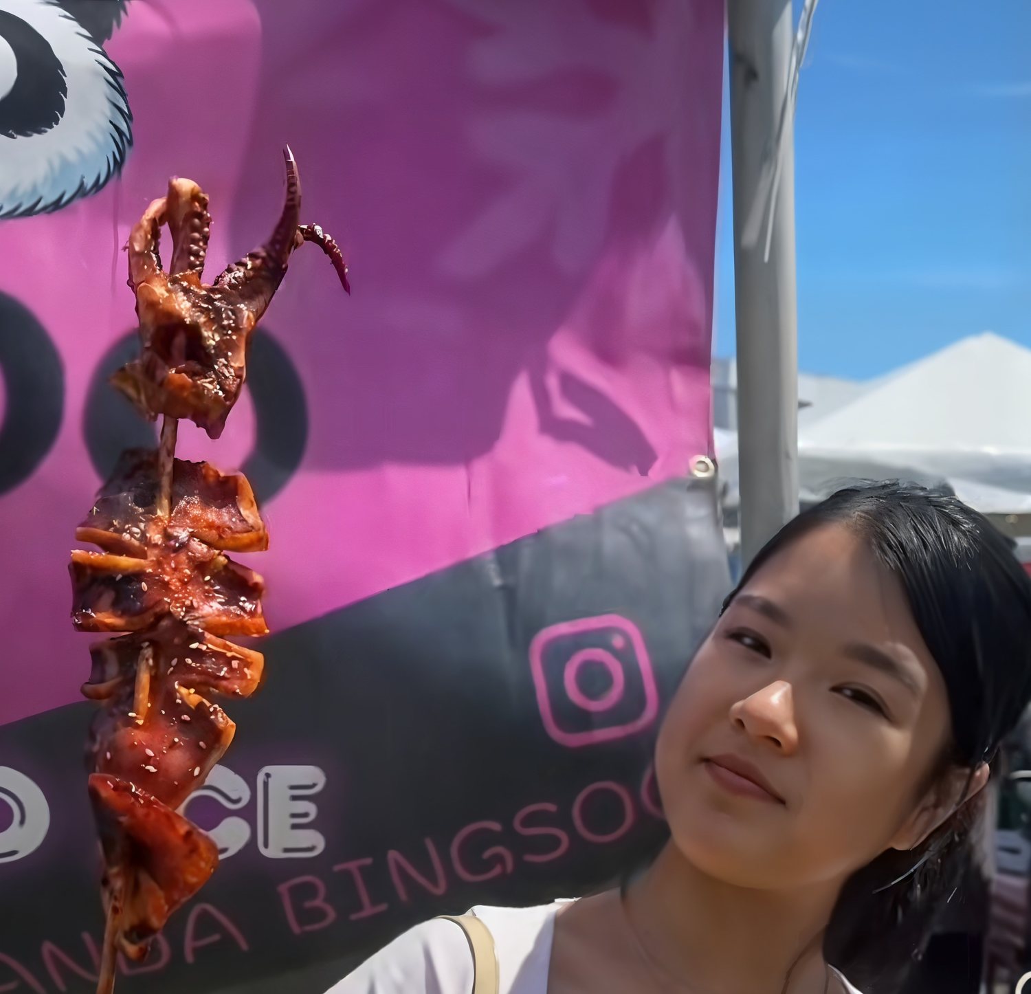 A festival-goer holding a chili-glazed grilled squid skewer at Panda Fest